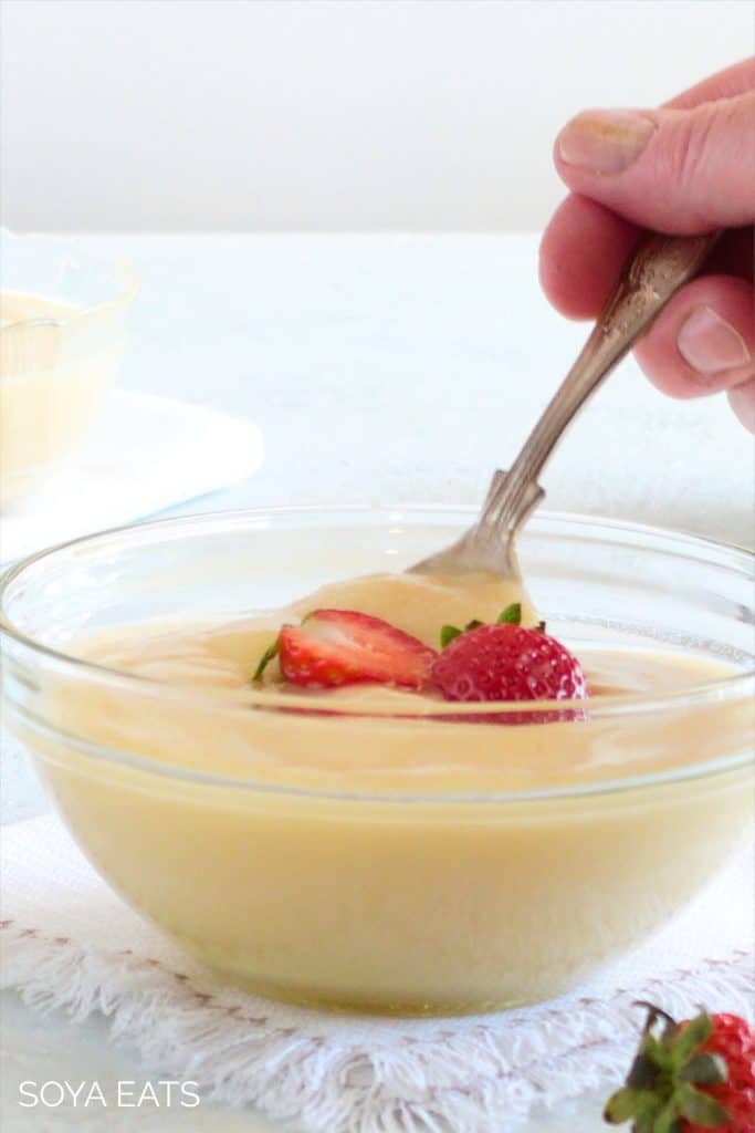 Hand holding a spoon in a bowl of custard.