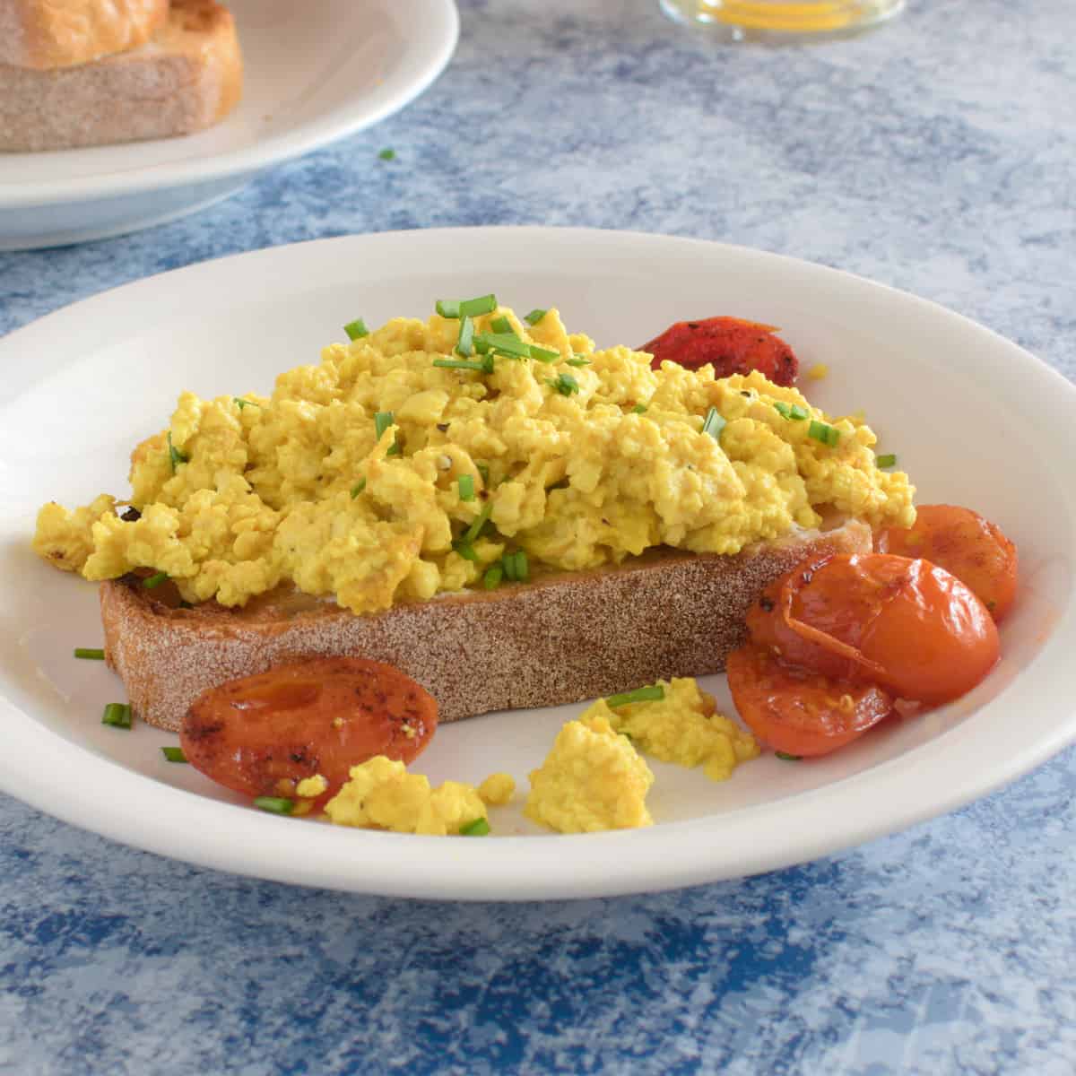 A breakfast plate of toast with scrambled silken tofu and pan fried tomatoes.