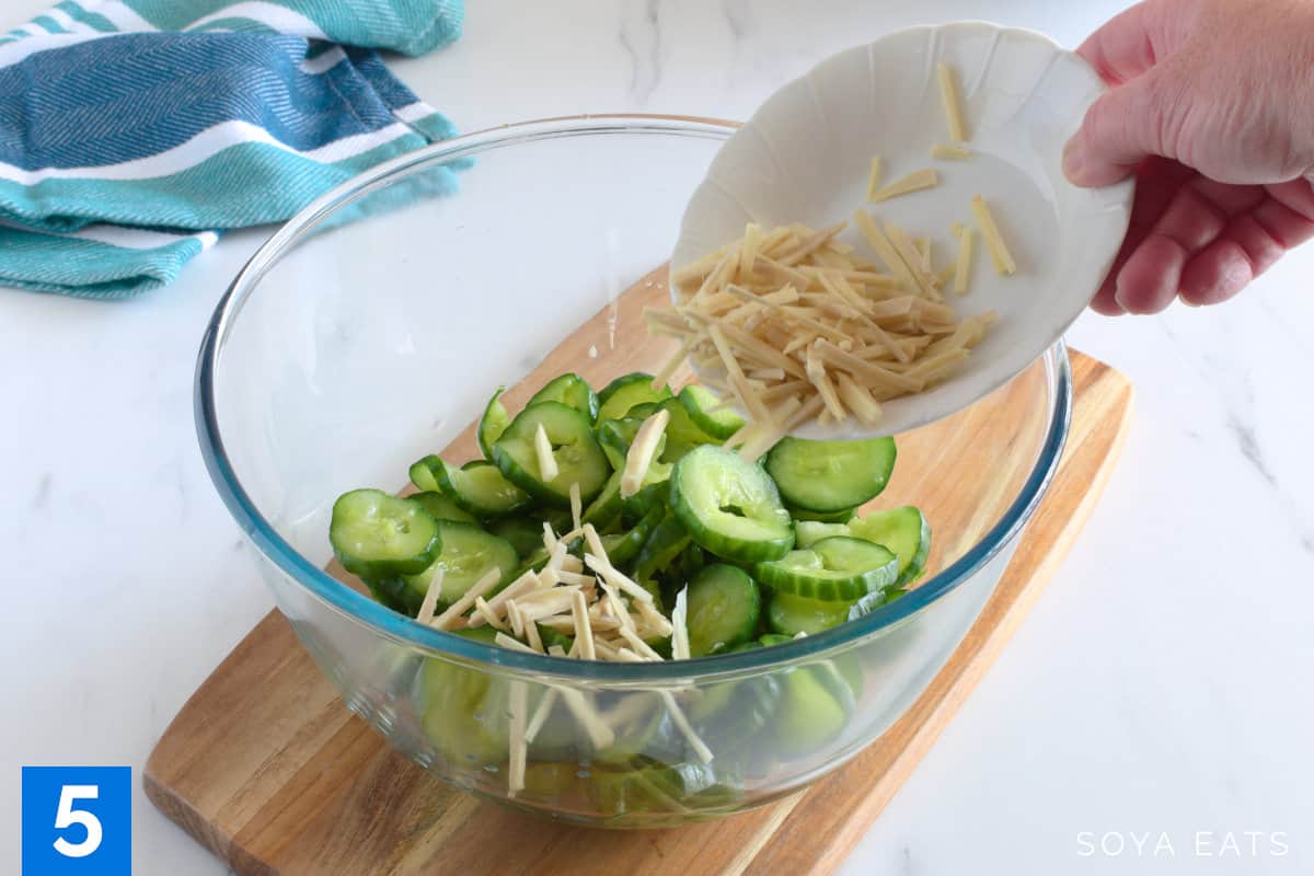Ginger pieces being added to a bowl with cucumber slices.