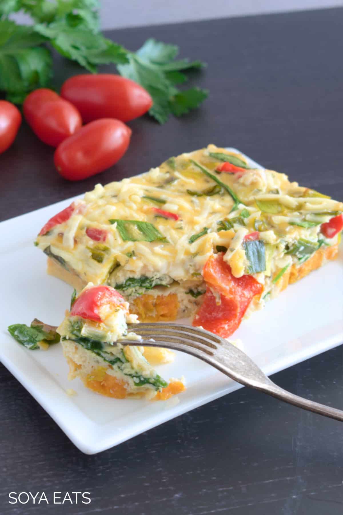 A slice of vegetable breakfast casserole with a fork on the plate.