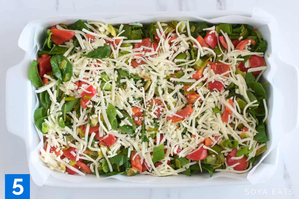 Vegetables for a breakfast casserole layered in a lined baking dish.