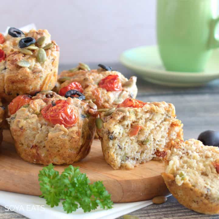 A close up of savory vegan muffins on a wooden board with a green mug in the background.