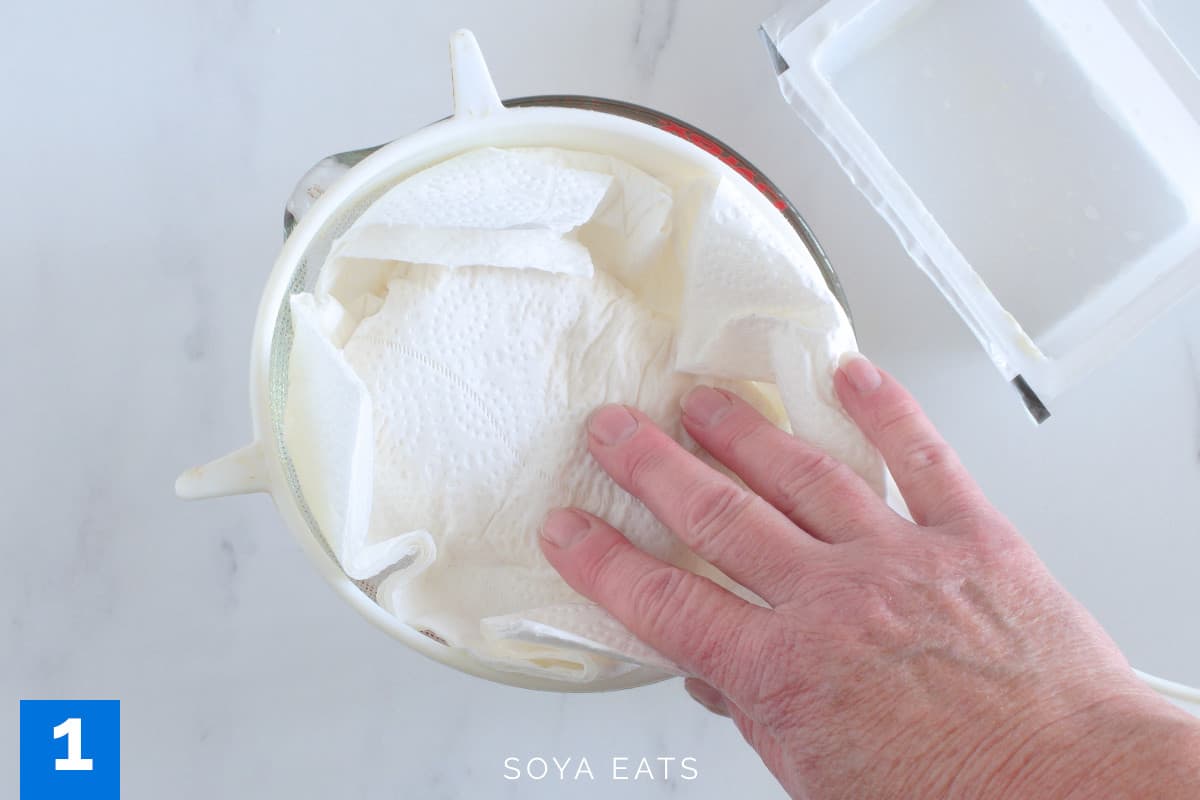 Silken tofu being drained with a strainer and absorbent paper.