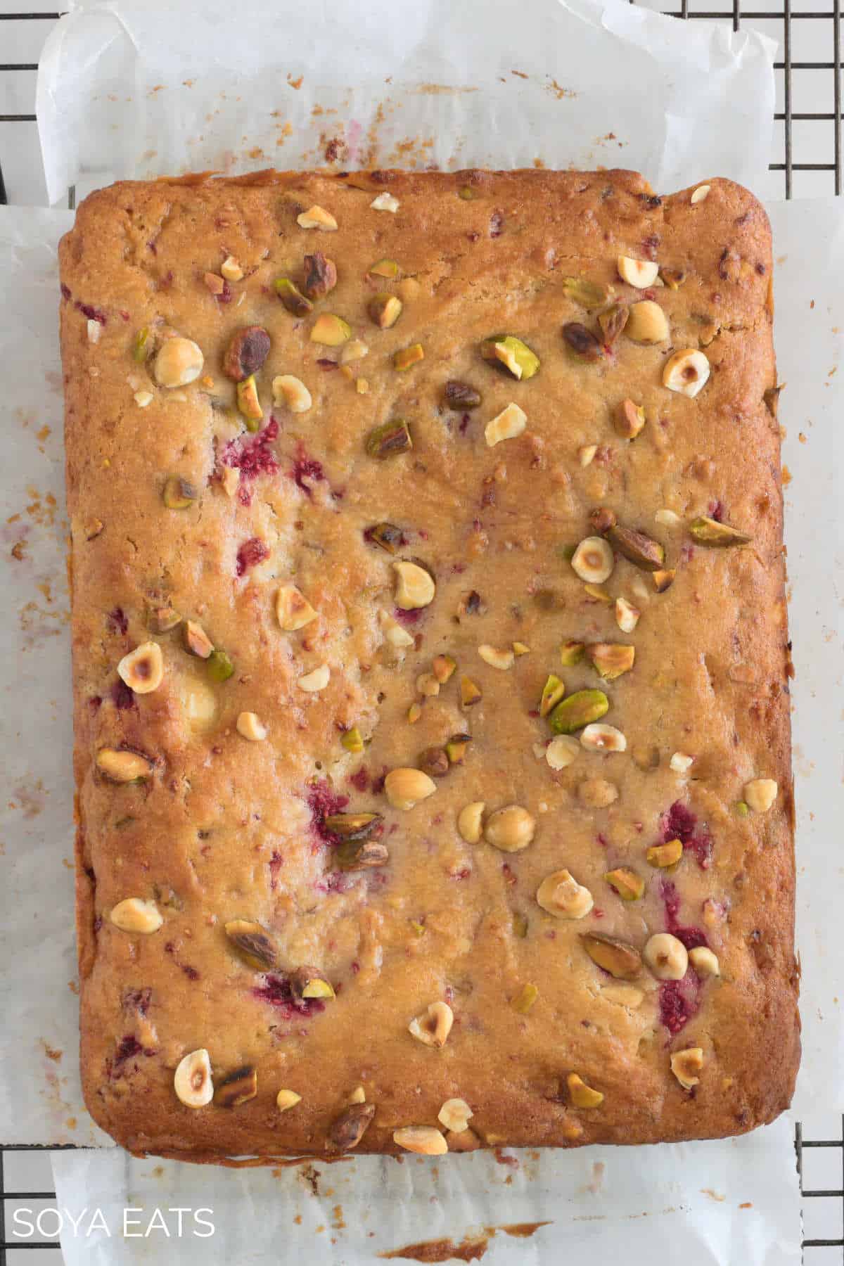 An uncut white chocolate and raspberry blondie on baking paper on a cake rack.