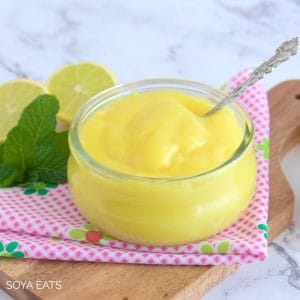Eggless lemon curd in a small glass bowl with a spoon in it.