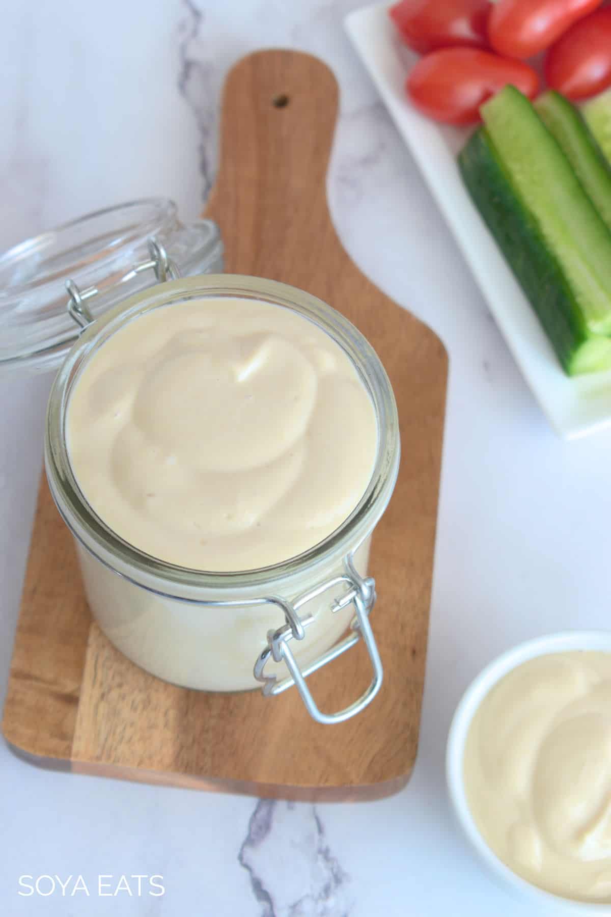 Top down view of homemade low fat vegan mayonnaise in a jar with vegetables in the background.